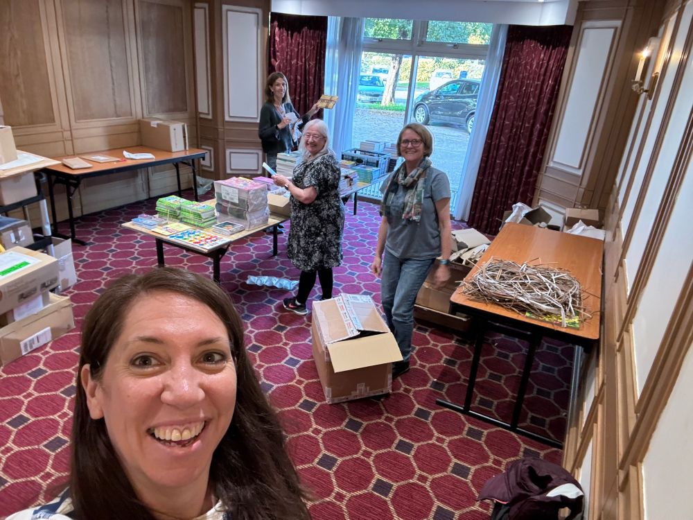 Four people in a hotel meeting room. They are packing conference goody bags. 