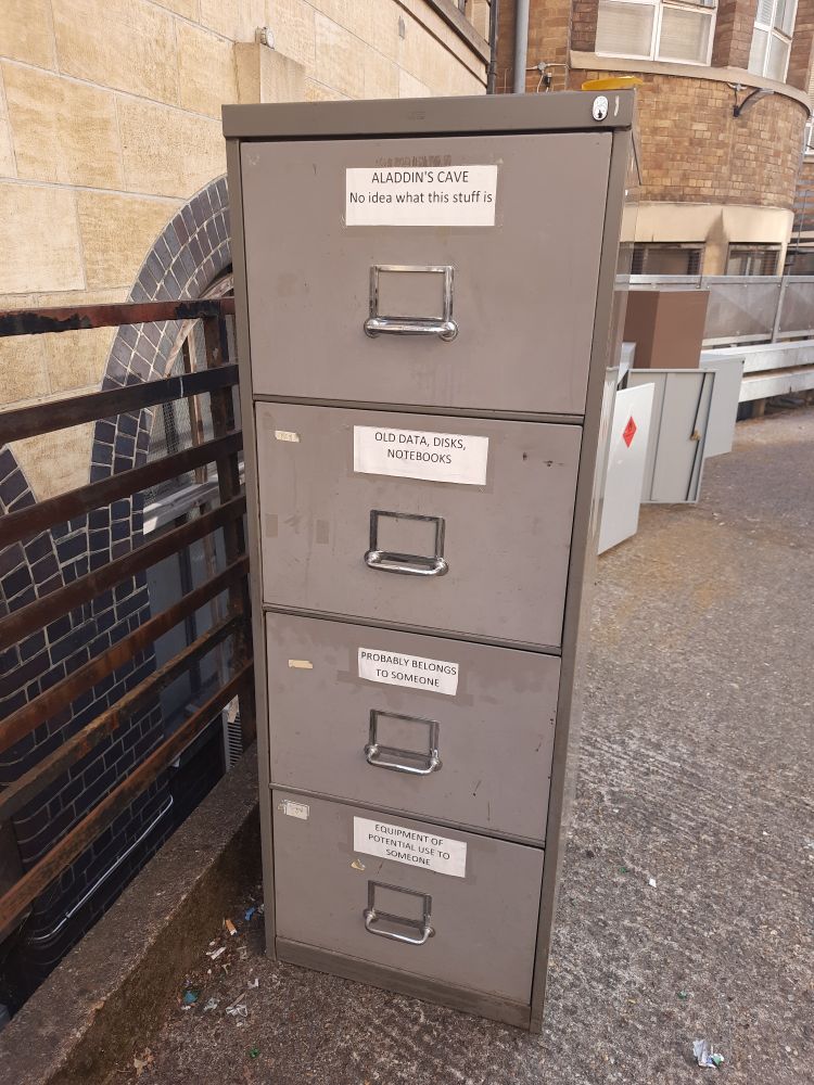 A filing cabinet outside a building. The drawers say: 'Aladdin's Cave (no idea what this stuff is', 'old data, disks, notebooks', 'probably belongs to someone' and 'old equipment that might be useful'.