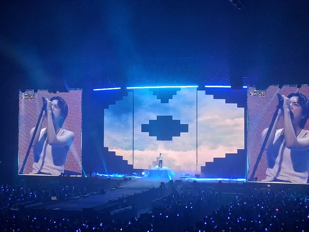 A picture of Jin singing on stage in a white tanktop at his last concert in Amsterdam. 