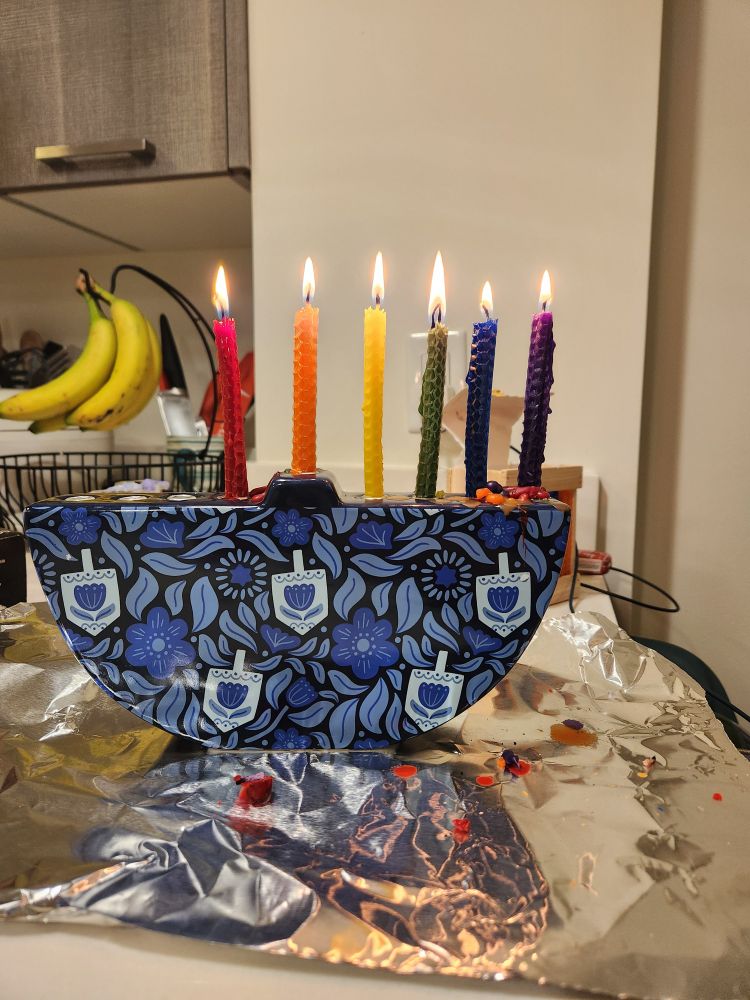 A menorah lit for the fifth night of chanukah. The candles have been arranged to make a rainbow.