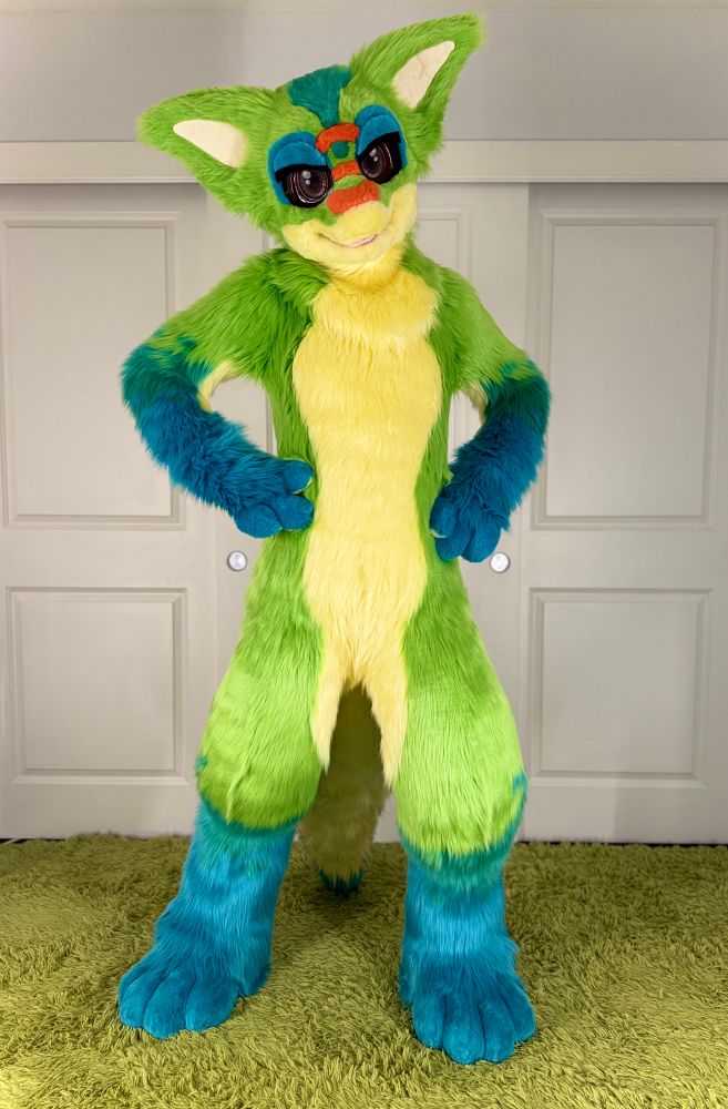 Basyl, a big eared, anthro day gecko stands atop greenery with his claws on his hips looking at the camera with big brown eyes. 