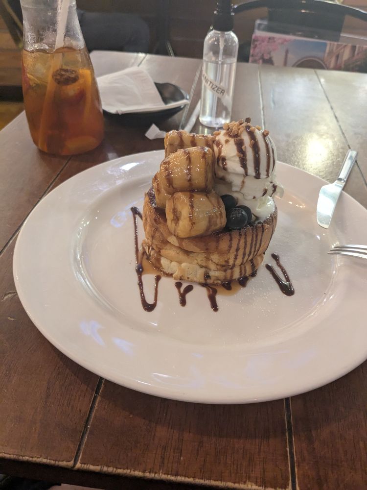 A banana caramel pancake drizzled with chocolate sauce with a vanilla ice cream on top. Next to it is a glass of fruit tea.