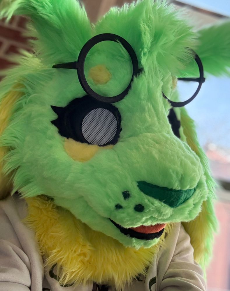 a photo taken of my sona skye, a green and yellow alien bunny inspired by a pair of ears that i got from beables baubles booth in 2024. skye is looking at the camera with her follow me eyes, her head facing towards the right side of the photo. 