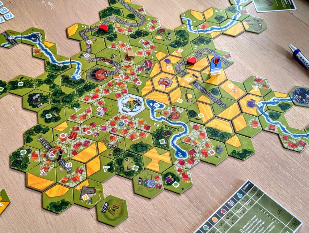 Overhead view of an ongoing board game of Dorfromantik, with the pieces assembled to form a large village.