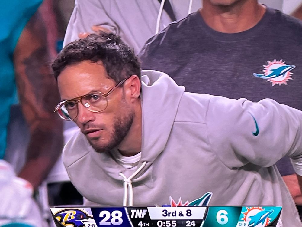 Coach Mike McDaniel leans over and forward, like he’s looking closely at something. 