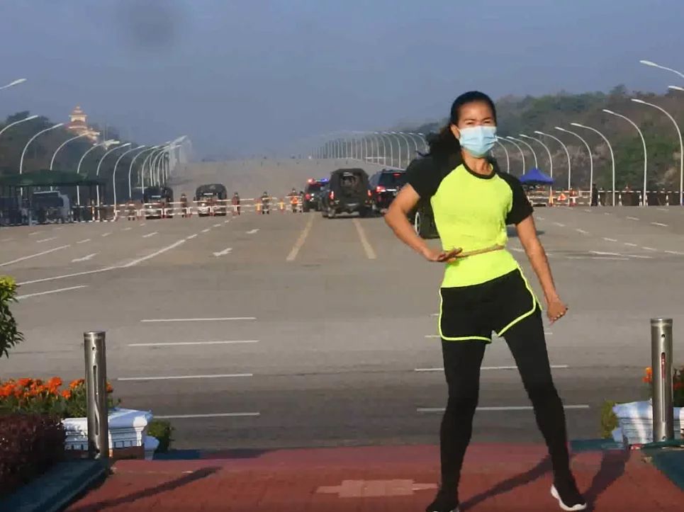 A woman does fitness dancing/exercises for the camera, seemingly not aware of the Myanmar coup happening in the background. 