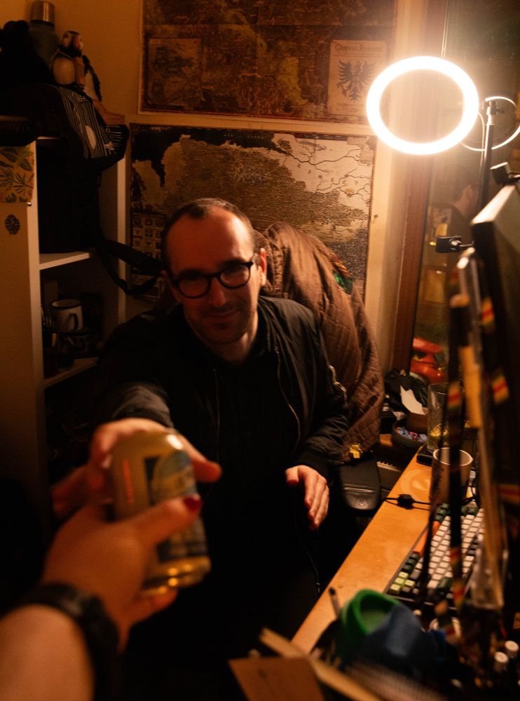 Someone sitting at a desk being handed a beer