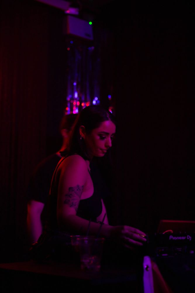 Single shot of a DJ in a washed pink light, extremely serene vibe that does not reflect the level of synth bangers she was dropping