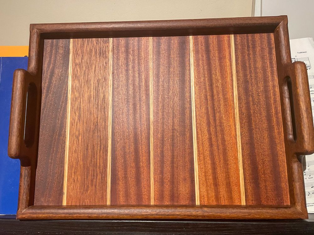 A photograph of a wooden tray.  The base is made from strips of alternating light and dark wood. 