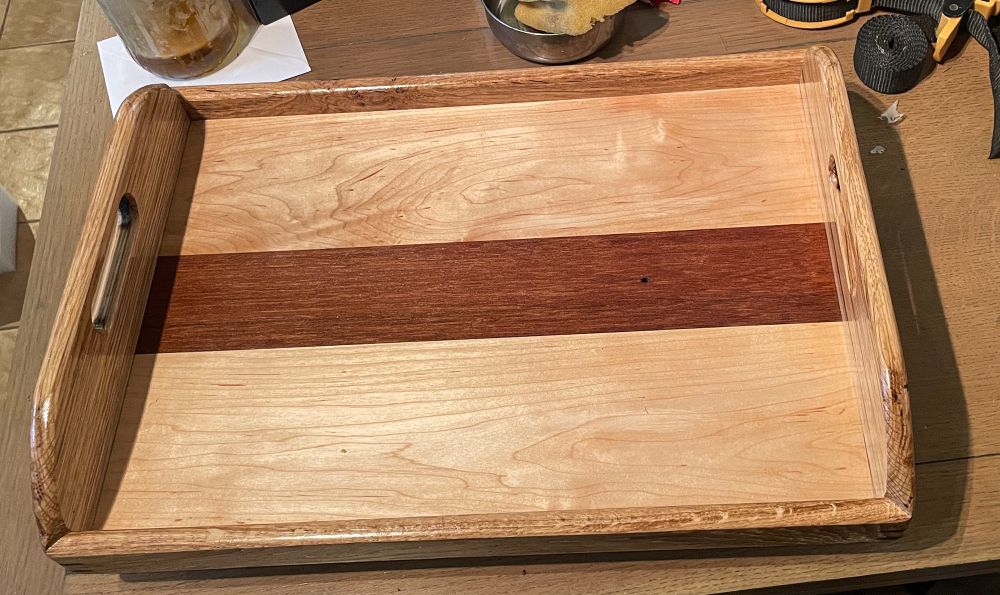 A photograph of a wooden tray. The handles are oak, the base maple with a meranti centre