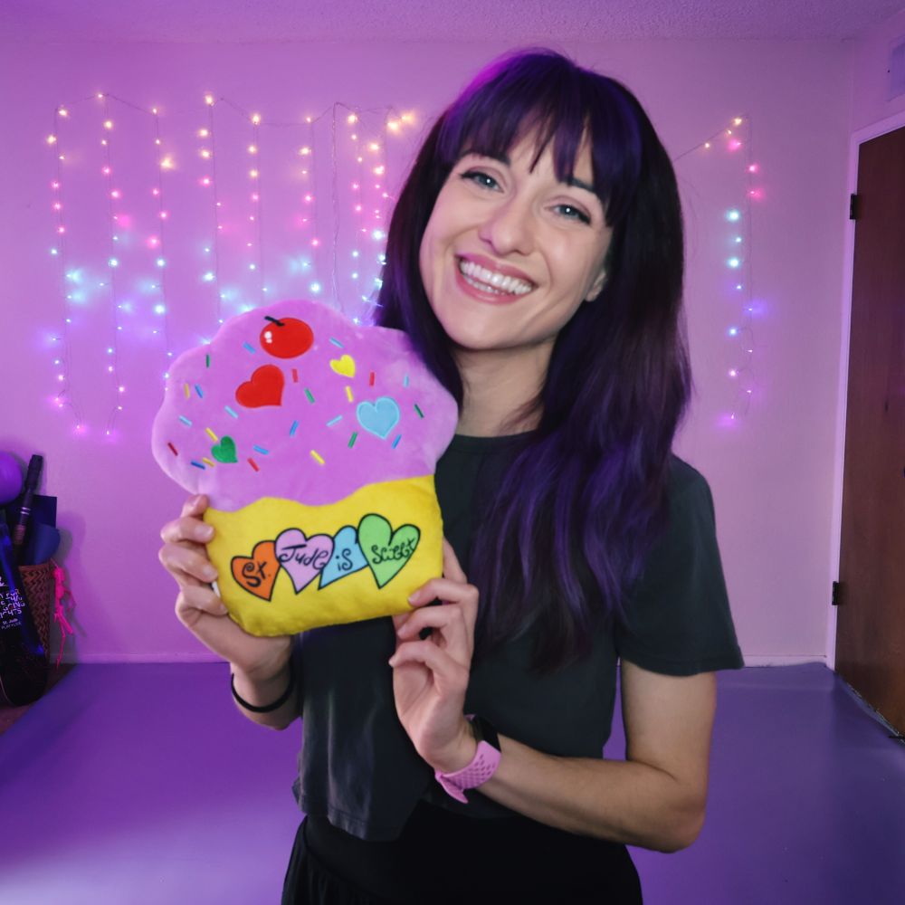 A selfie of meowtropolis smiling and holding a cupcake plushie that says "St. Jude is sweet"