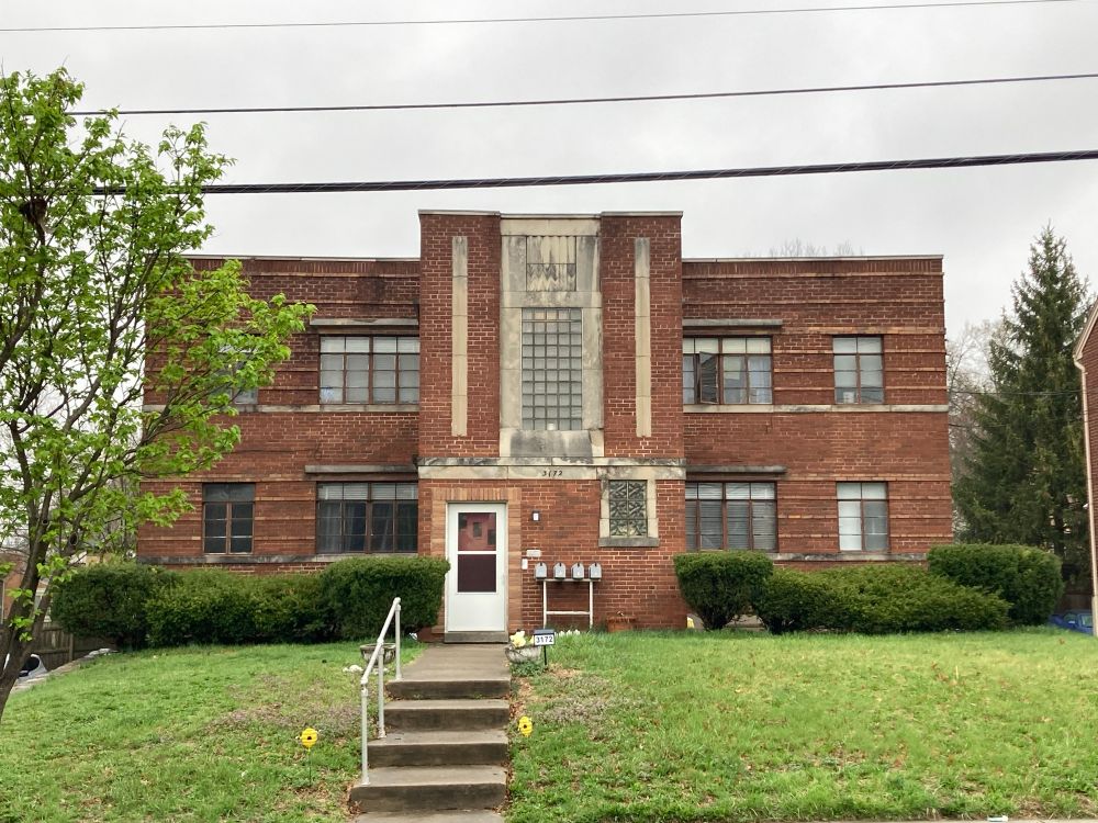 Another symmetrical, squat, two-story duplex set off the street by a suburban lawn. This one features prominent ornamentation on a front piece that protrudes from the otherwise rectangular building.