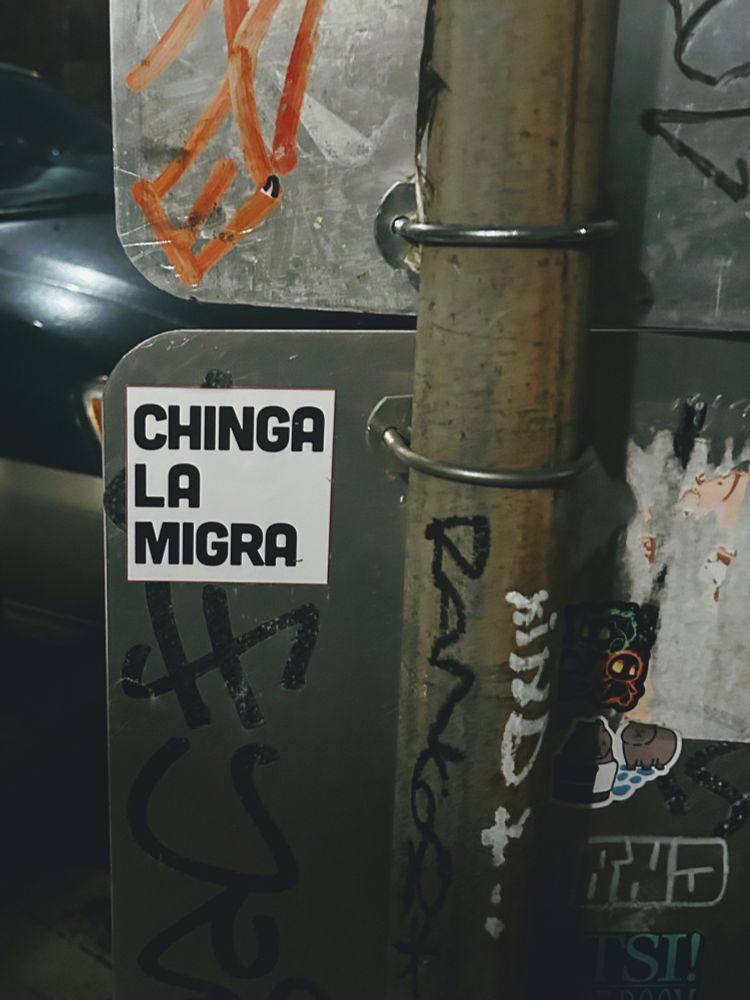 Sticker on the back of a parking sign that reads in Spanish “Chinga la Migra”