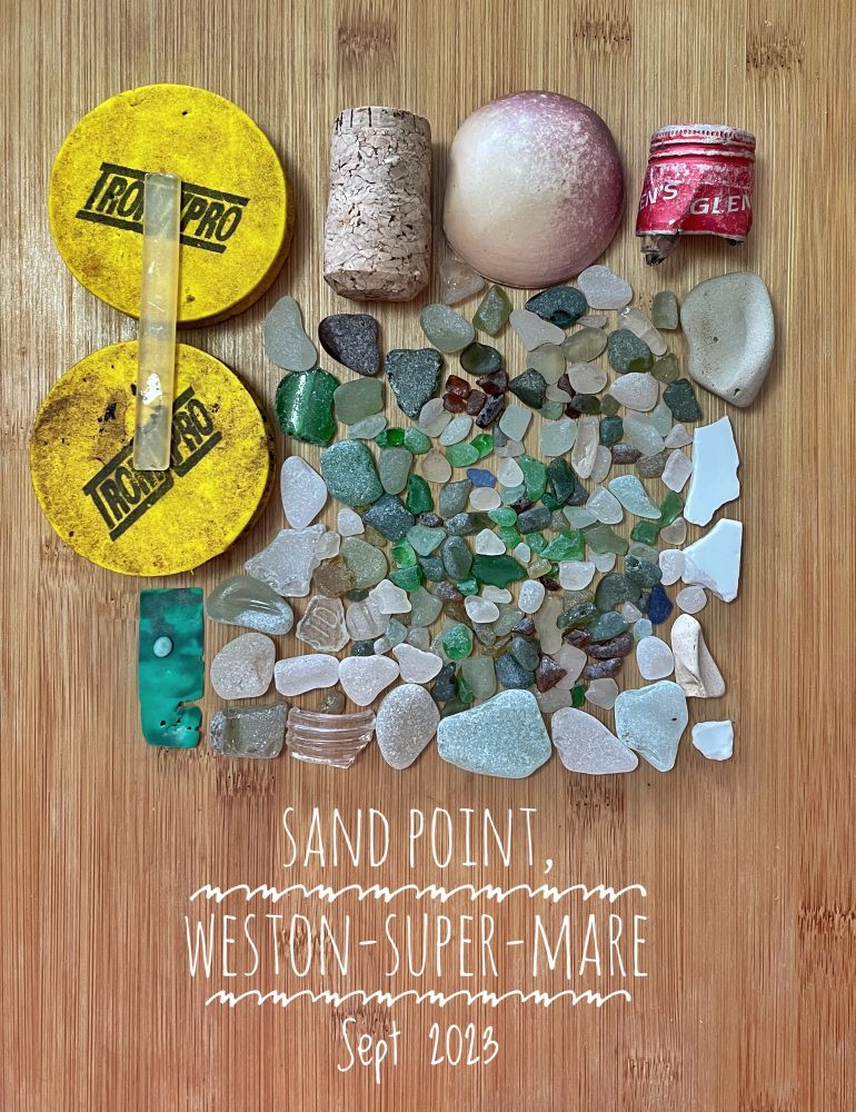 Beachcombed objects laid in a square shape on a woodsurface. Dozens of pieces of seaglass in various shades, two large yellow plastic objects, and other miscellany. Text reads sand point, Wesson super mare, sept 2023