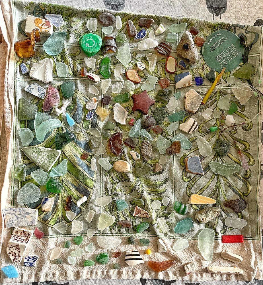 Dozens of beachcombed finds, mostly seaglass and seapottery, laid out on a tea towel
