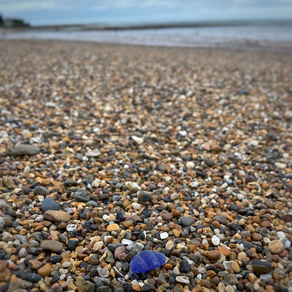 The blue seaglass in context - it is low foreground and a shingle breach stretches to a grey blue sea