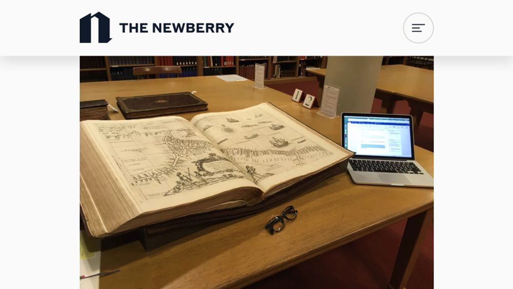 A large book of maps on a table with an open laptop computer and a pair of glasses.