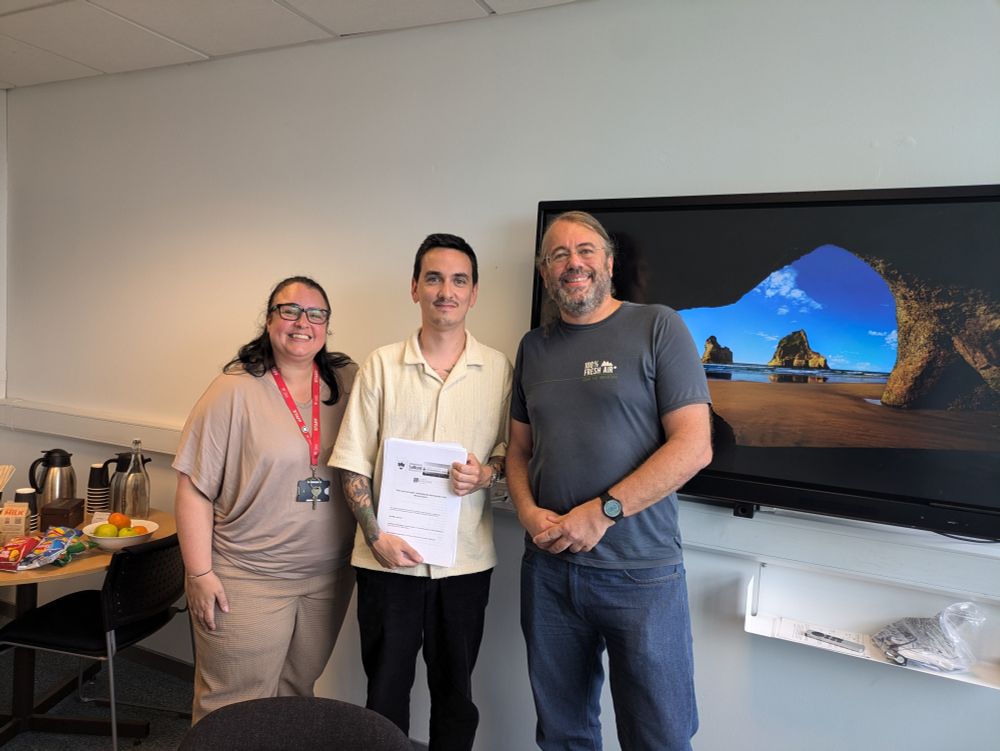 Jake holding his thesis with the internal and external examiner
