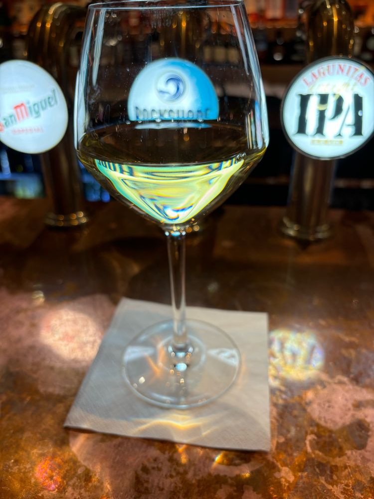 A glass of Chablis (white wine) on a white napkin, sitting on a brown bar. Behind the glass are beer taps for Lagunitas IPA, Rockshore, and San Miguel.