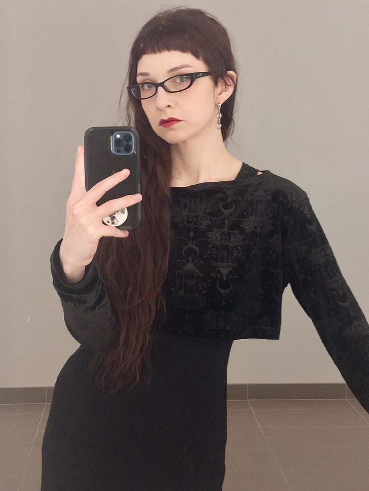 mirror selfie: white woman with waist-length wavy red-violet-brownish hair, Bayonetta glasses, and sick-as-fuck all-black outfit that involves a printed velvet crop top over a dress. spiked chain earrings. microbangs. a nose that communicates clearly There Has Been No Nose Job Here. there’s a moon popsocket on the phone being used to take the picture. 