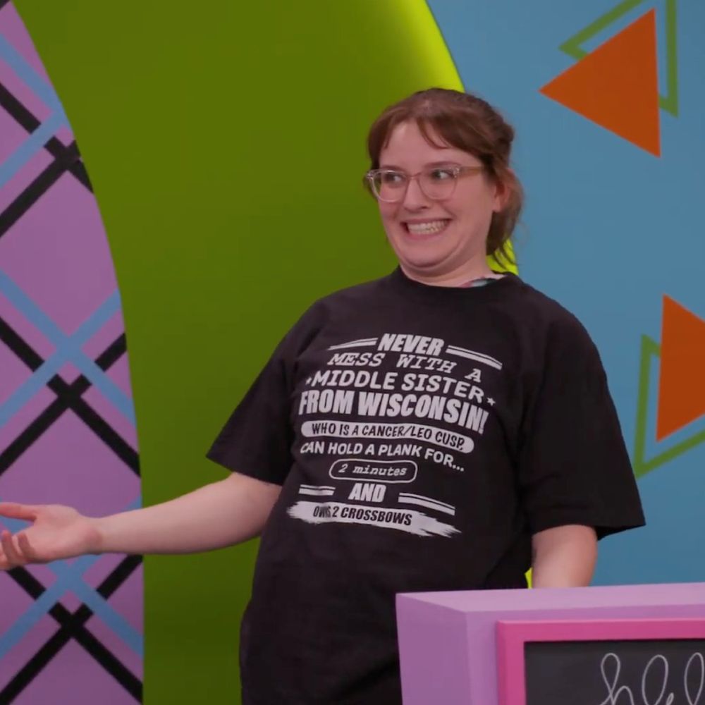 Izzy Roland smiling ear to ear wearing a shirt that says "Never mess with a middle sister from Wisconsin who is a Cancer/Leo cusp, can hold a plank for 2 mins, and owns 2 crossbows".