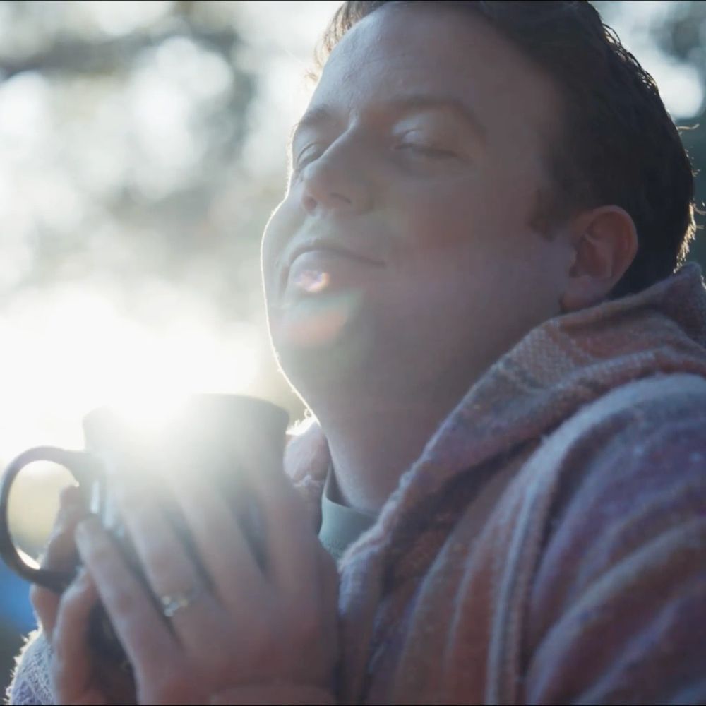 Brennan Lee Mulligan cherishing a warm cup of coffee outdoors in the morning light.