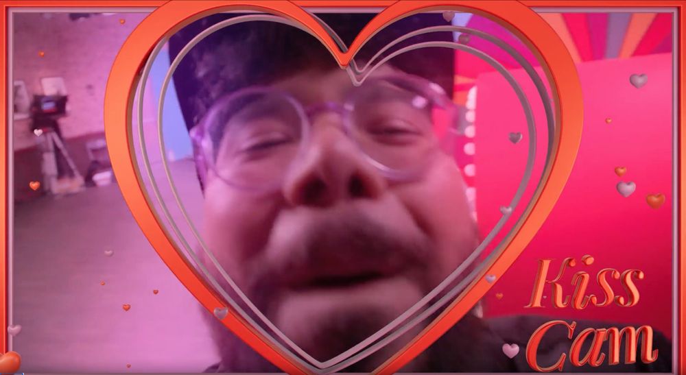Closeup shot of Oscar Montaya approaching the Kiss Cam to kiss it without any teeth showing.