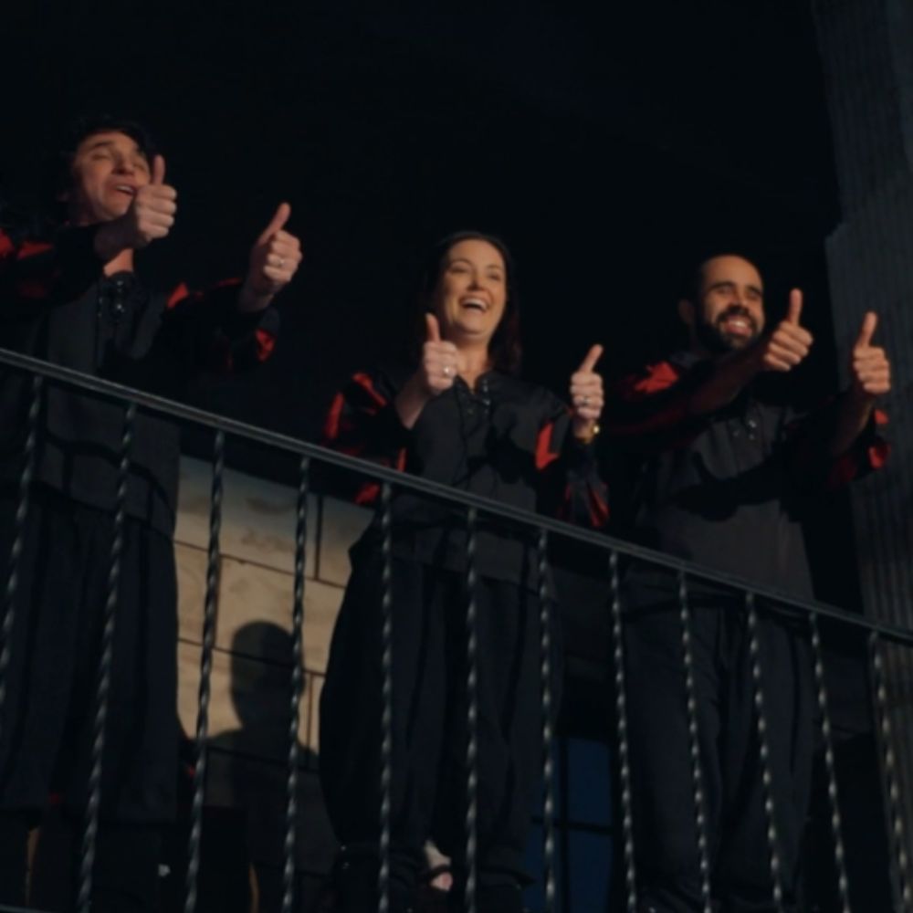 The cast of 'The Official Cast Recording' all giving thumbs up from a balcony. Sam Reich is completely enamored at the sight.