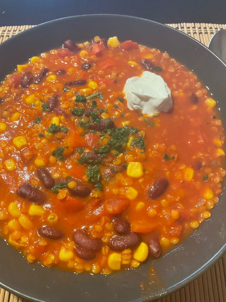 Teller mit Chili ein Carne aus roten Linsen mit einem Klecks Creme Vega und etwas Petersilie.