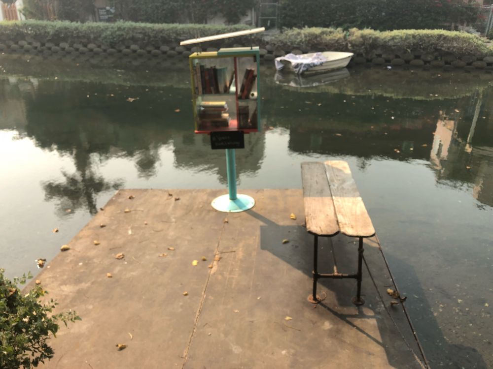 A little free library on a small dock, with a bench, on a canal in Venice, CA