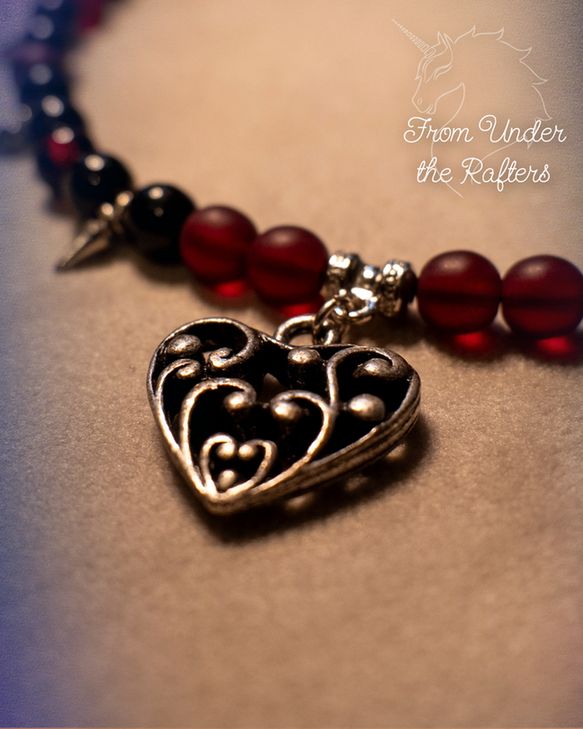 Detailfoto van een bedel aan een ketting met rode en zwarte kralen.