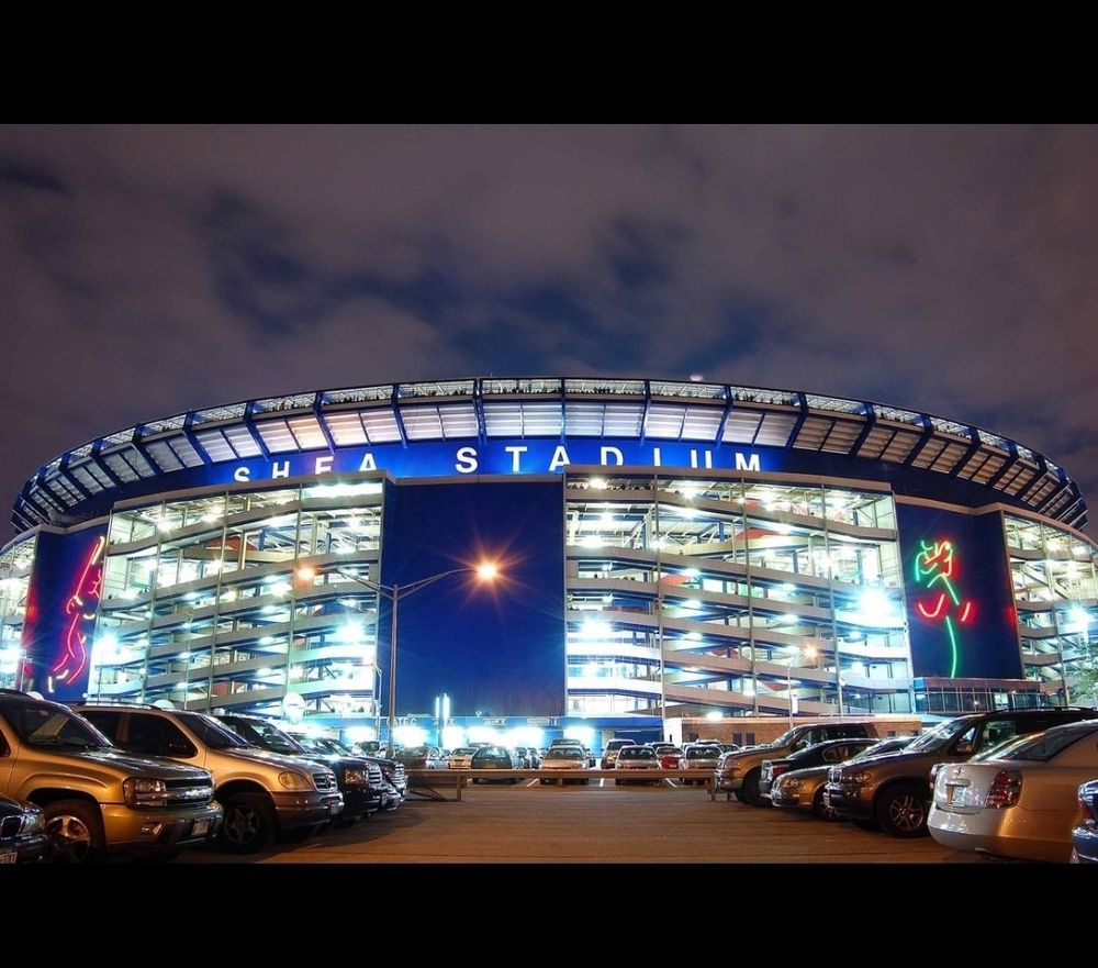 Shea stadium lit up at night viewed from the parking lot on a cloudy night. 