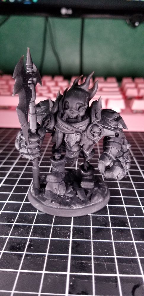 Photo of Lil Skeleton Boss Gary. A 75mm tall miniature of a Dullahan styled skeleton. Flames erupt from a human skull in the eyes, wreathing the head in flickering flames around the skull. Gary is carrying a halberd with larger, almost boxing sized metal gloves. Skulls and spikes adorn the chest plate he now wears. A simple scarf, loin cloth, and boots are the only other clothing worn. He stand with one leg slight behind himself and one leg on a stump or larger rock from the base.