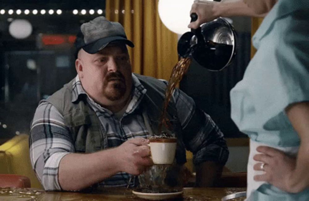 a man is pouring coffee into a cup while wearing a baseball cap