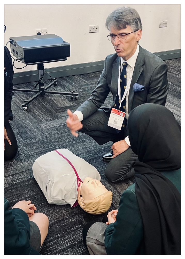 A medical professional demonstrating CPR using a medical mannequin to a group of school children
