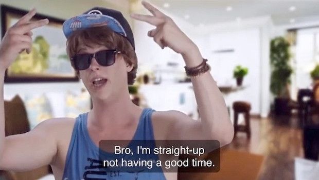 A meme of a young man (zoomer?) with a mop of brown hair, indoors in a blue tank top, sunglasses and flat brim baseball cap, flashing "deuces" or peace signs with each hand, saying "Bro, I am straight-up not having a good time." 