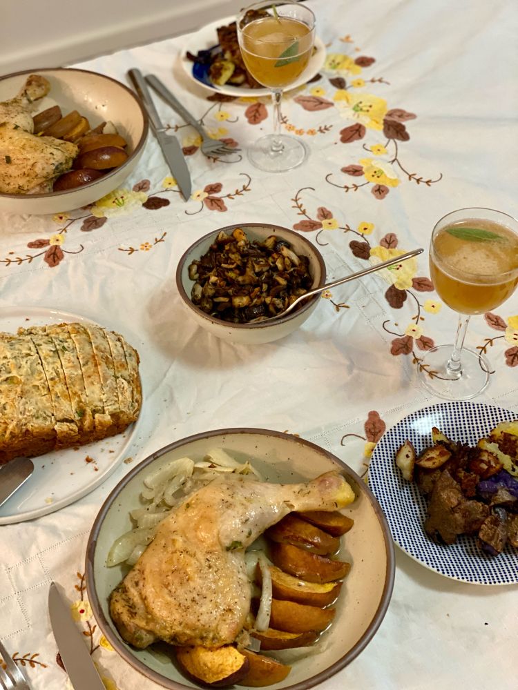 A floral table cloth with several food dishes and two cocktails.