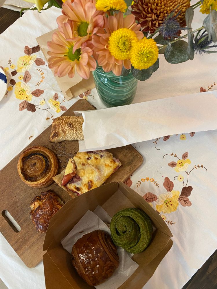 6 pastries on a wooden chopping board on top of a white table cloth with flowers. 