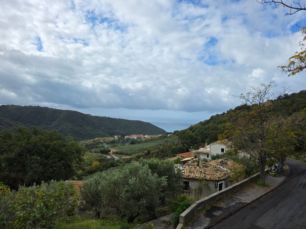 Green valley home to houses with clay tile roofs, with the sea in the background.