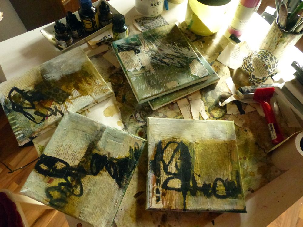 Ein Tisch im sanften Morgenlicht, auf dem kleine Mixedmedia Arbeiten liegen, die noch fertiggestellt werden müssen.