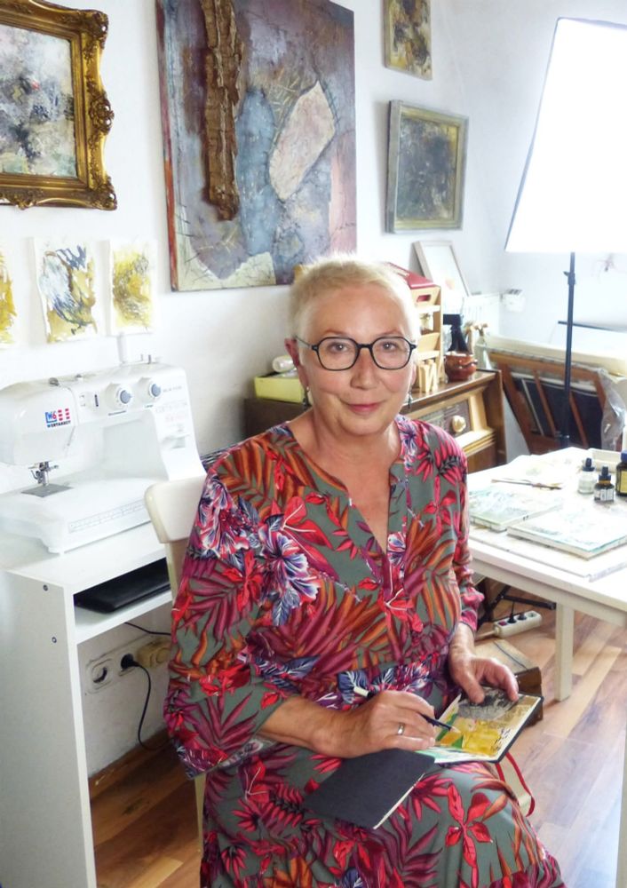 Ich -  in einem geblümten Kleid - in  meinem Atelier. Im Hintergrund Arbeitstisch, Künstler Materialien und eine Nähmaschine.