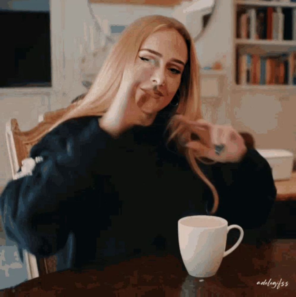 a woman in a black sweater sits at a table with a cup of coffee