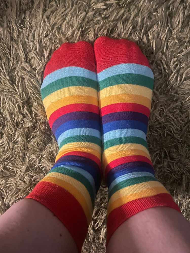 Regenbogen-Ringelsocken, zwei Füße auf grünlichem Teppich