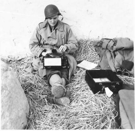 A man sits on straw with a typewriter.