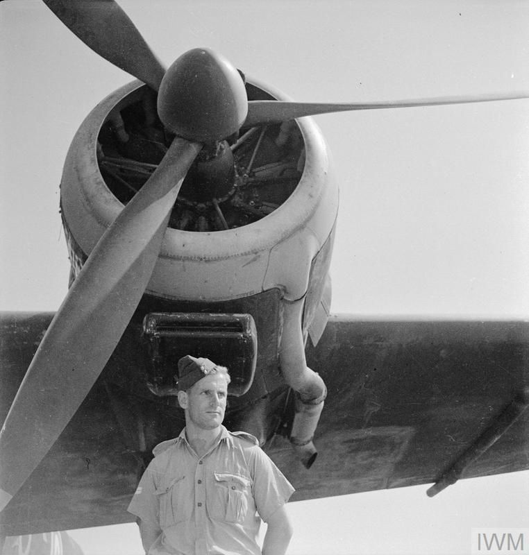 A man in uniform stands underneath the propellor of an aircraft.