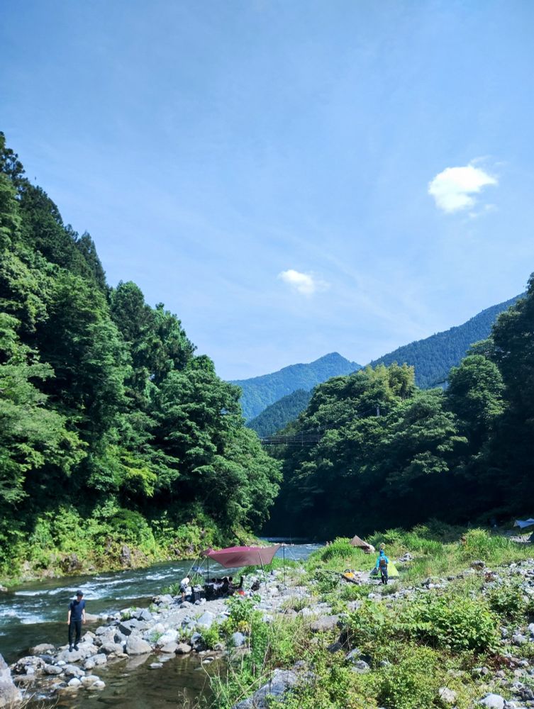 A riverside mountain valley campsite with green mountains and Bluesky in the background.