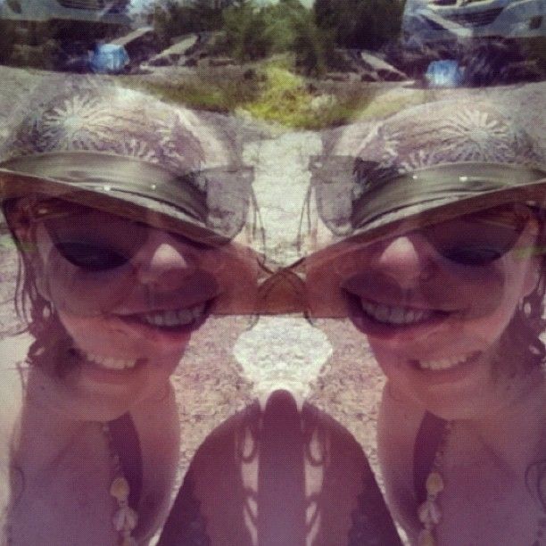 A double and mirrored exposure of 2 friends smiling in sunglasses and a straw hat with a green ribbon band.
