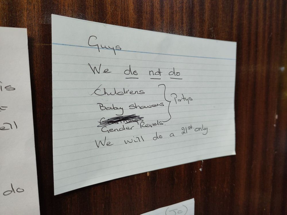 Small handwritten sign next to a bar saying "Guys We do not do Childrens Partys Baby Showers Gender Revels (sic) We will do a 21st only"