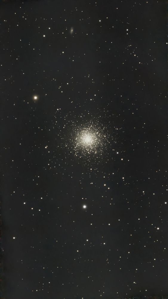 A dense ball of stars is positioned in the centre of the image. Other stars are scattered around it. At the top of the image and slightly to the left you can make out the faint smudge of a distant galaxy