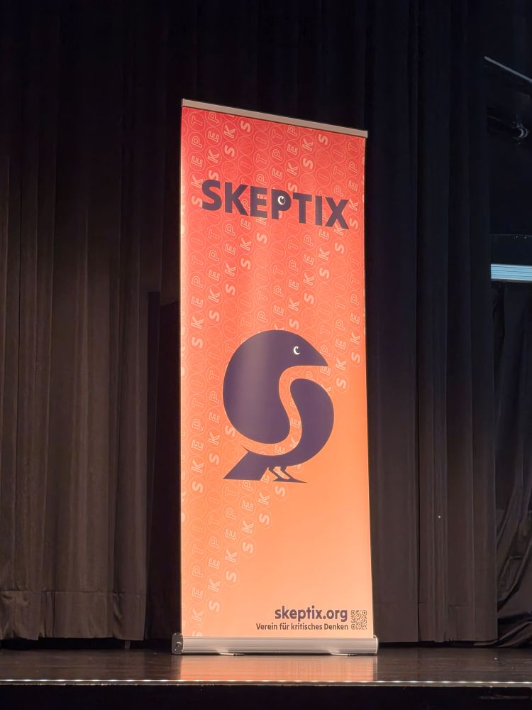 Orangener Aufsteller des Vereins "Skeptix". Text unten: "skeptix.org. Verein für kritisches Denken"